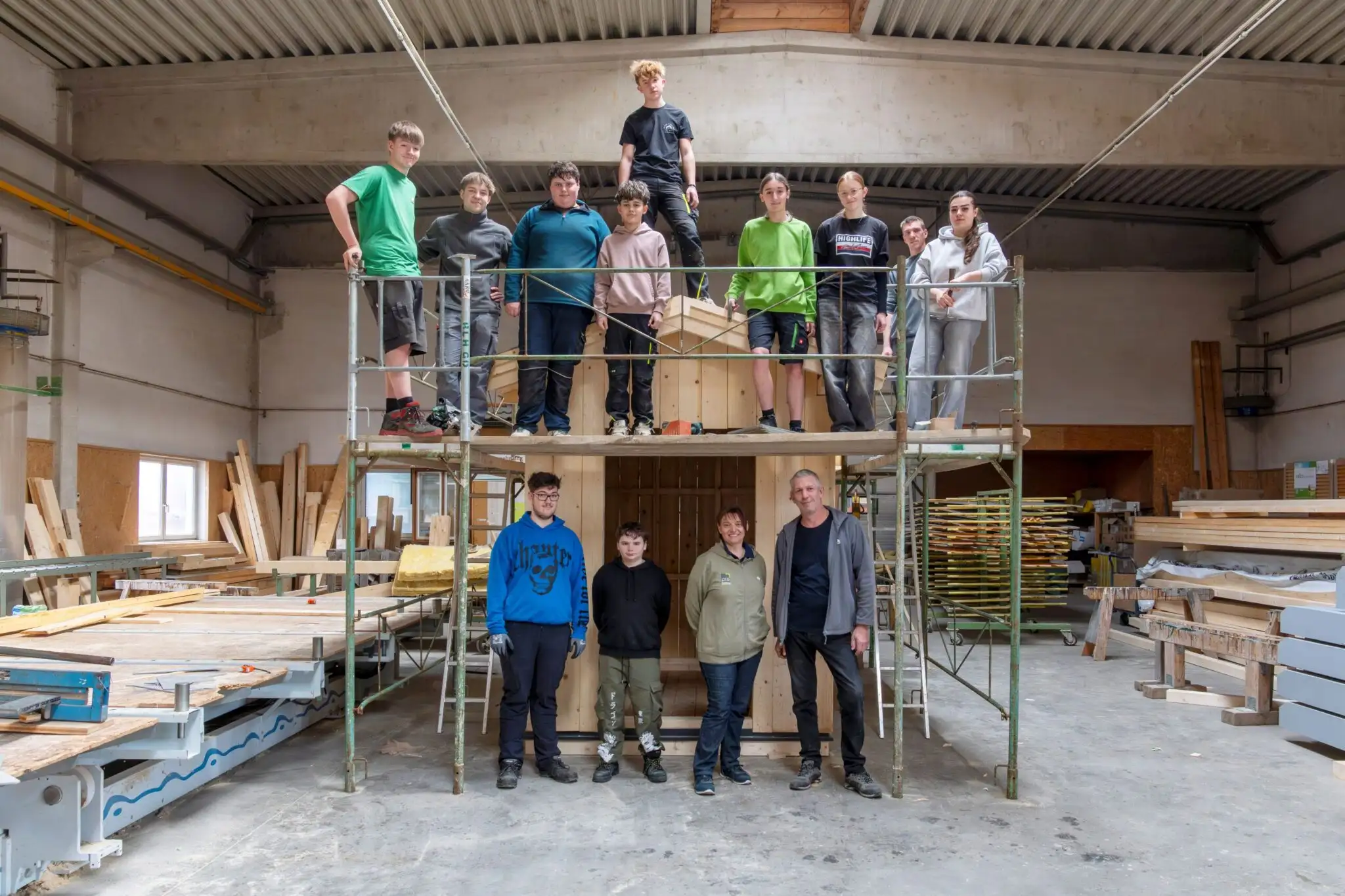 Die Schülergruppe steht auf einem Gerüst in einer Werktstatt.