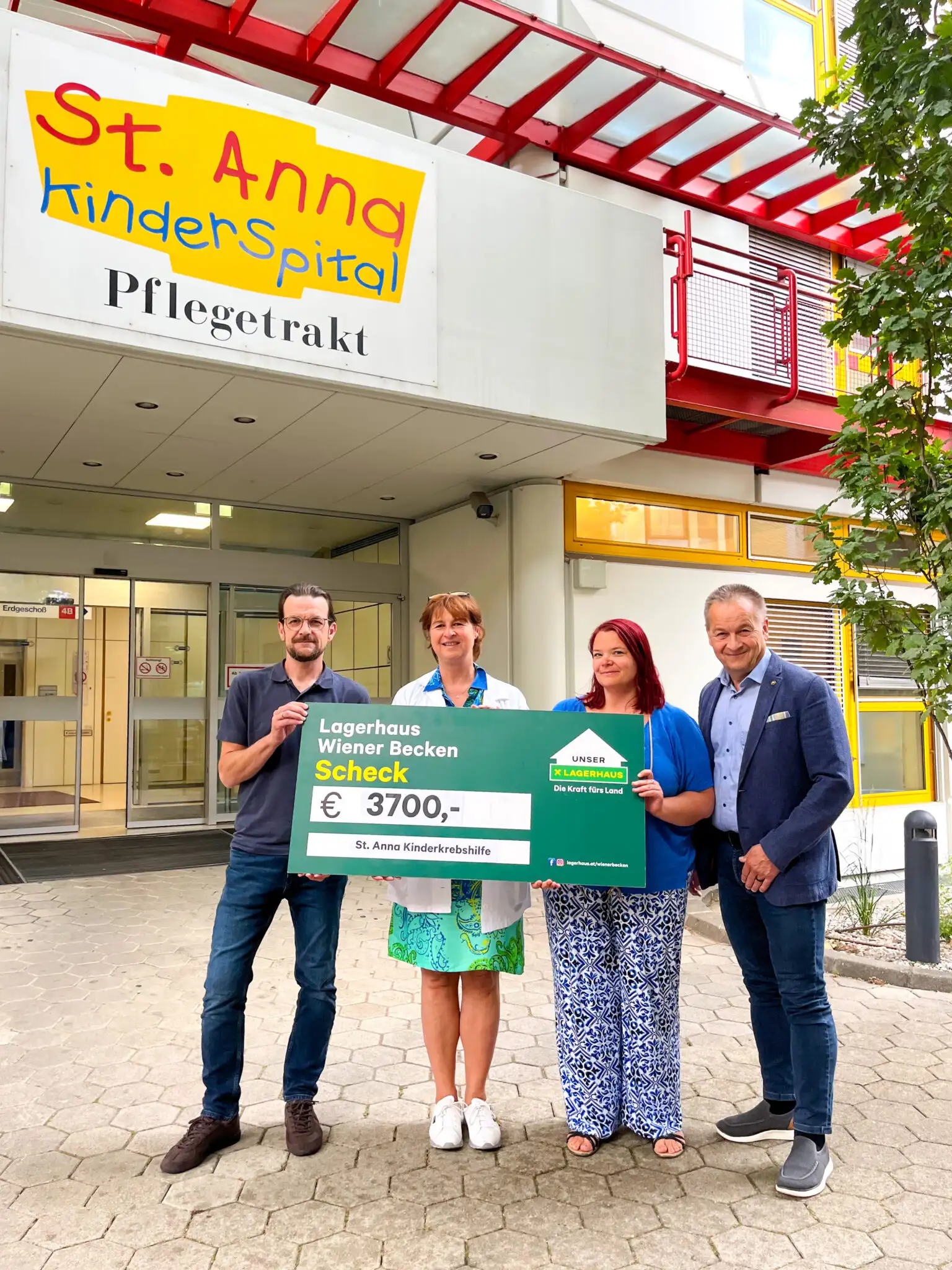 Übergabe des Spendenschecks vor dem Eingang des St. Anna Kinderspittals